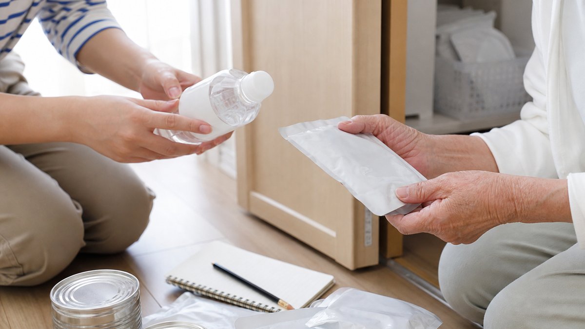 押し入れから出した保存水とレトルト食品の期限を確認する、親子の手元