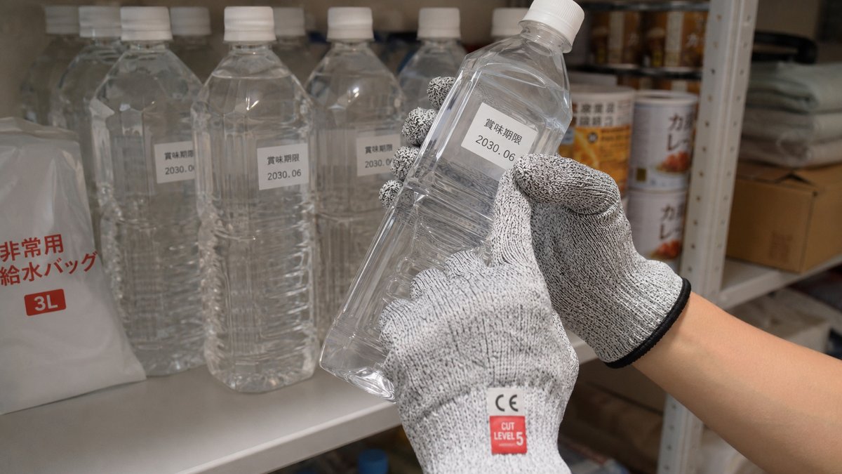 備蓄している保存水の賞味期限ラベルを手袋をつけた手で確認しているところ
