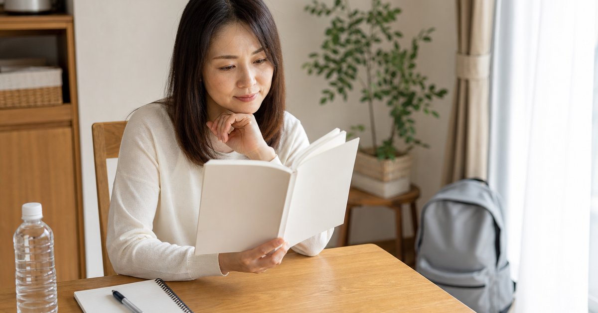 ダイニングテーブルで本を開き、防災について静かに考えている女性